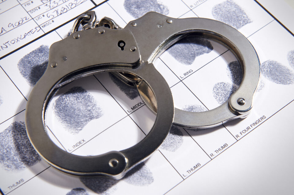 Metallic handcuffs placed on a fingerprint card, symbolizing law enforcement and drug crime defense