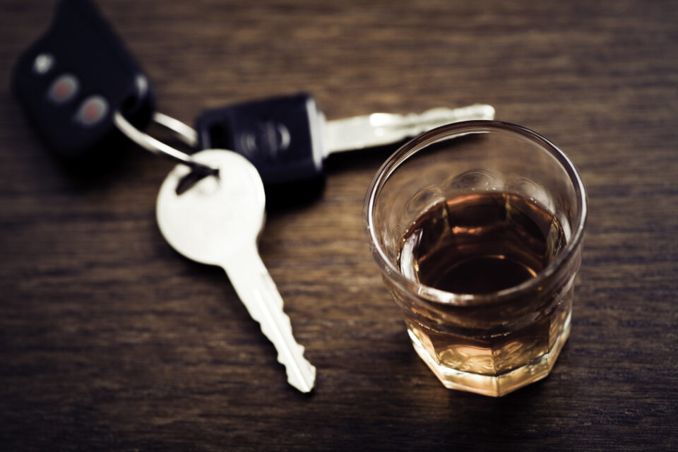 Car keys next to a glass of amber liquid on a wooden table, symbolizing the risks of drinking and driving
