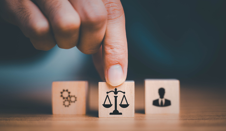 Hand adjusting a wooden block with scales of justice icon, symbolizing legal balance and fairness, alongside blocks representing processes and individuals, highlighting race discrimination advocacy.