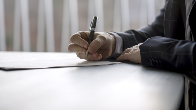 Close-up of a professional in a business suit signing legal documents at a desk, symbolizing the probate process and estate administration